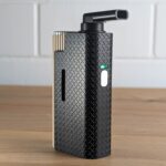 Der Frolic Thermal Extractor steht auf einem Holztisch. Im Hintergrund ist eine unscharfe weiße Backsteinwand zu erkennen.