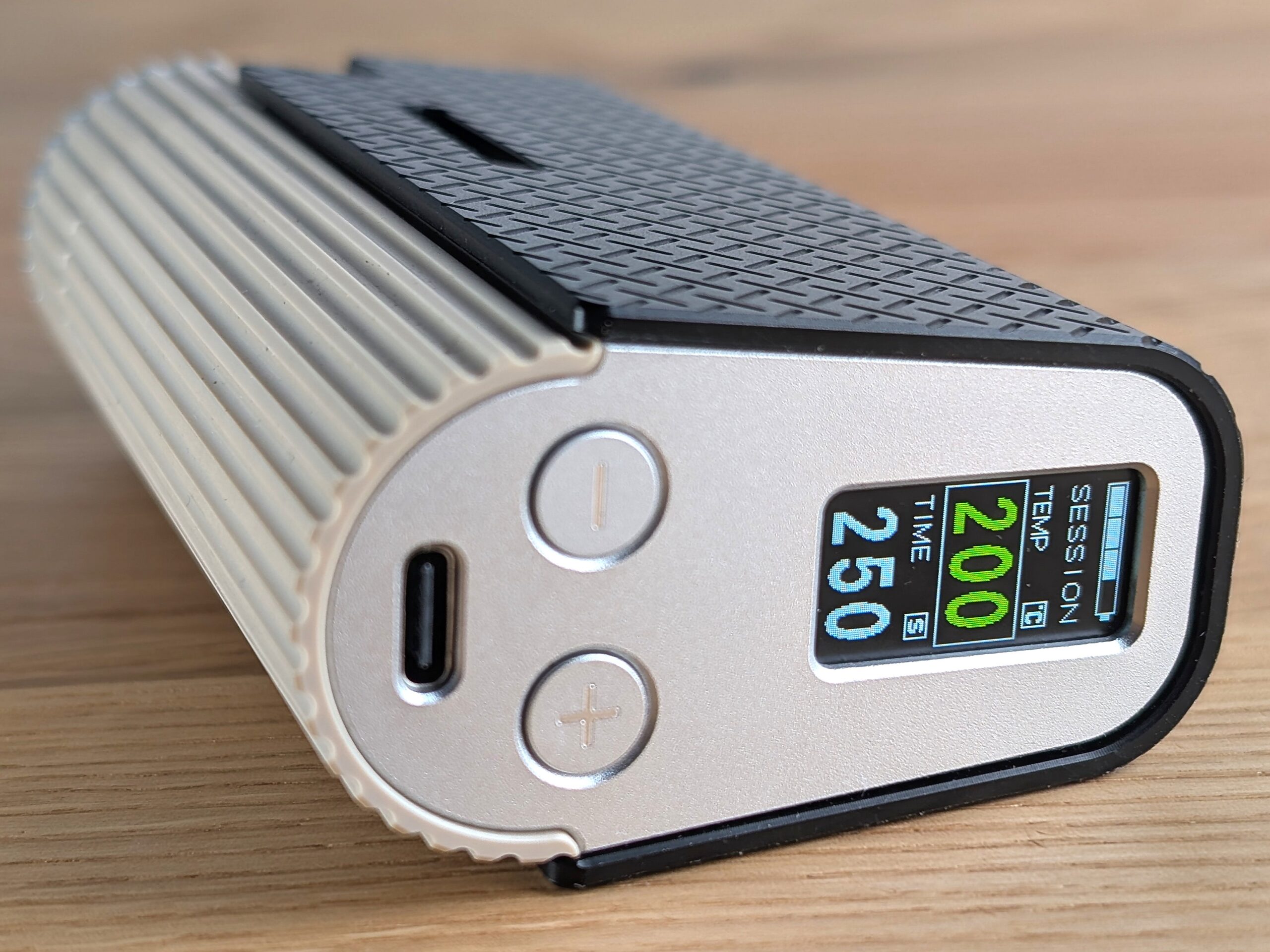 Der Frolic liegt seitlich auf einem Holztisch. Die Unterseite zeigt zum Betrachter. Auf der Unterseite sind das Display, die beiden Bedienungstasten und de USB-C Port zu erkennen.