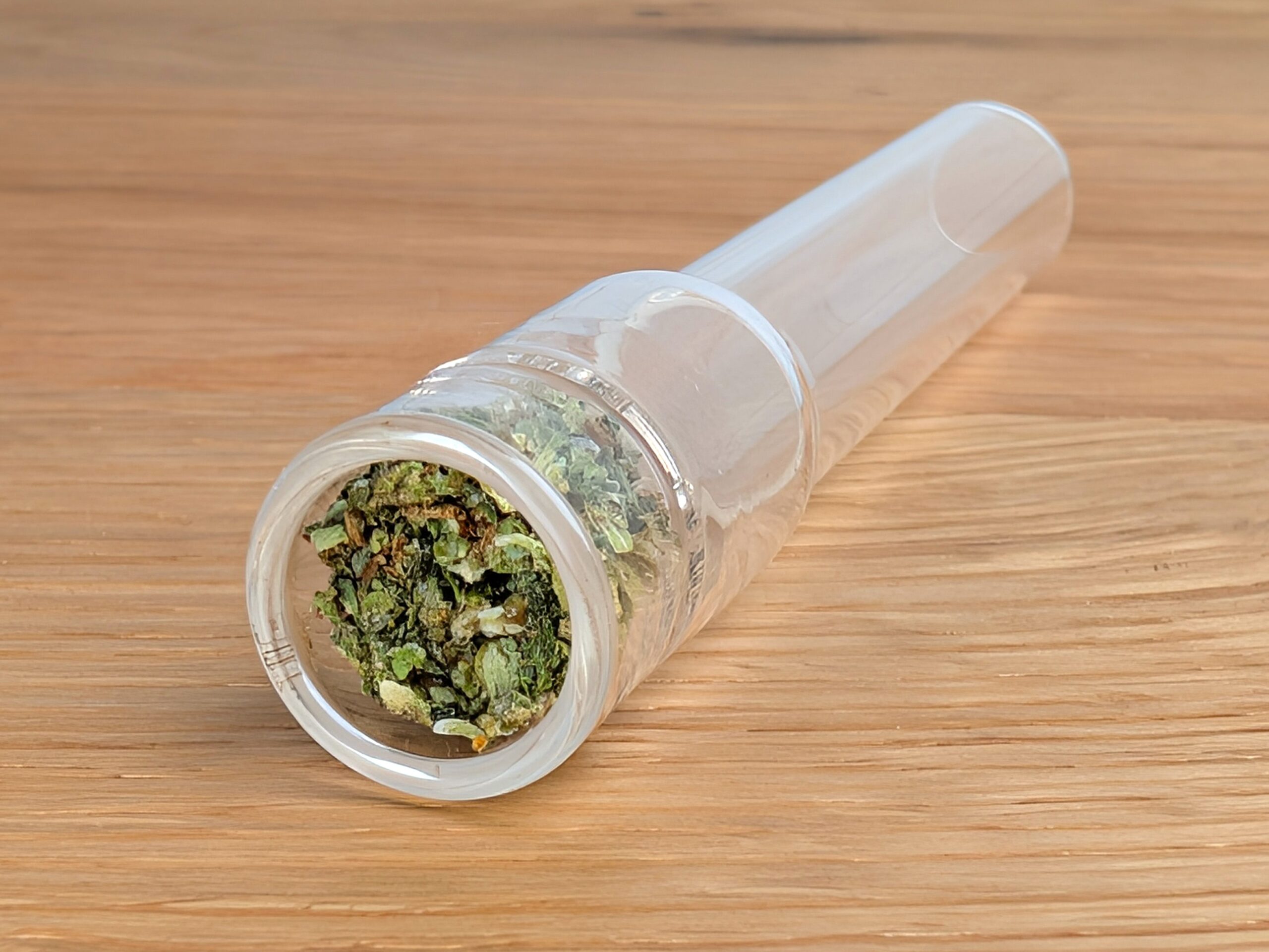 The image shows an Arizer stem filled with herbs, lying at an angle on a wooden table.