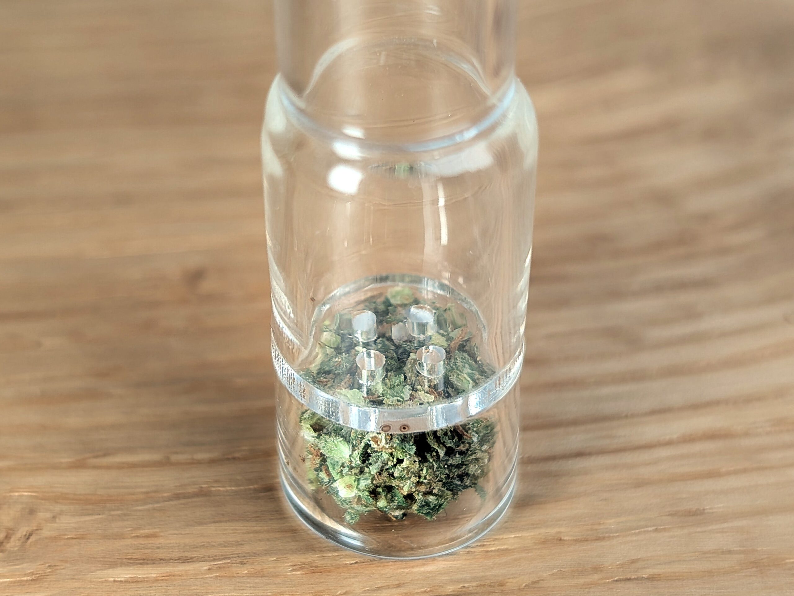 The image shows an aesthetic close-up of an Arizer stem filled with fresh herbs on a stylish wooden table.