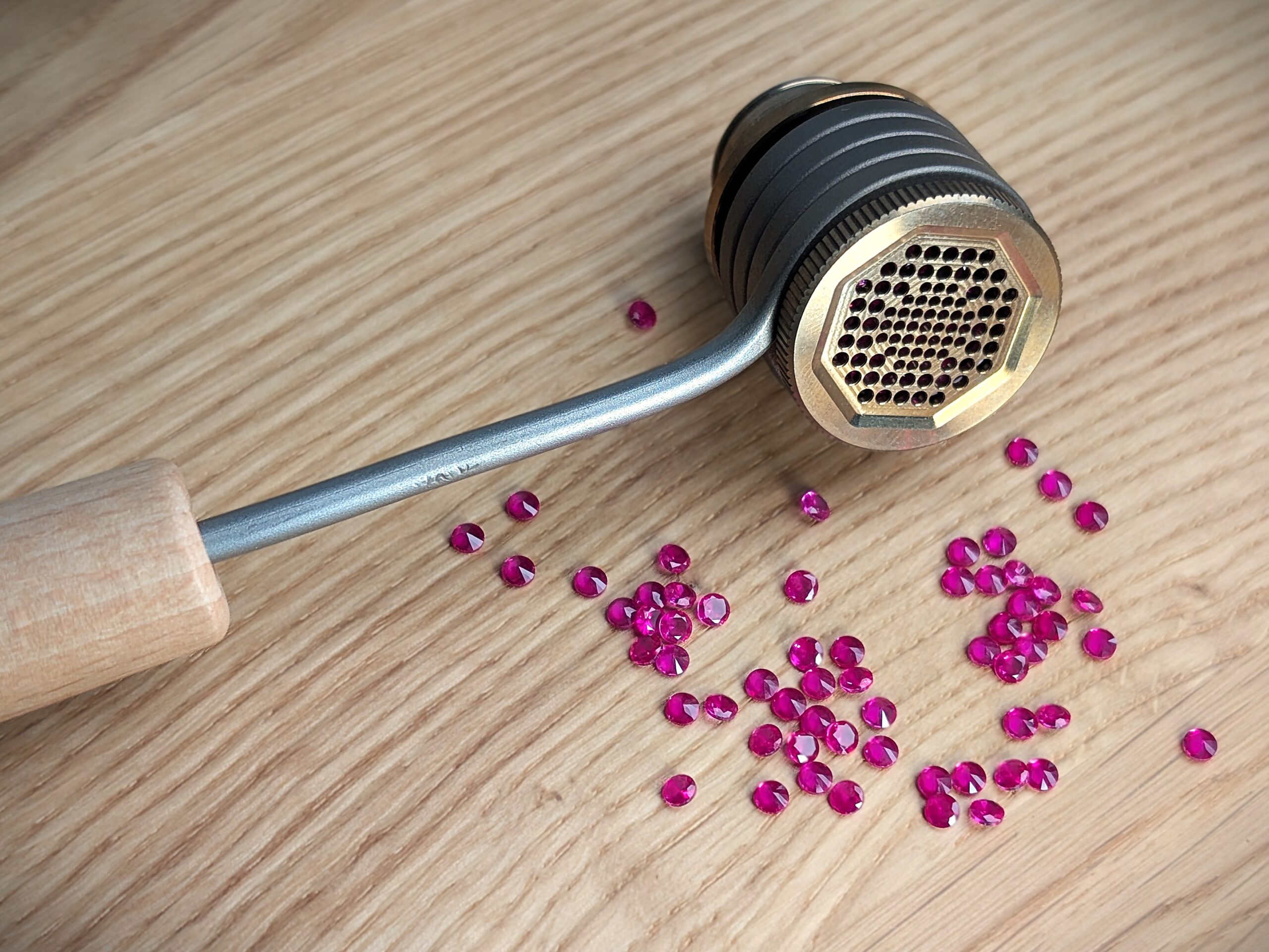 Close-up of a ball vaporizer on a wooden table. The heating coil of the vaporizer and part of the wooden handle are visible. About 30 artificial rubies are placed in front of the vaporizer.