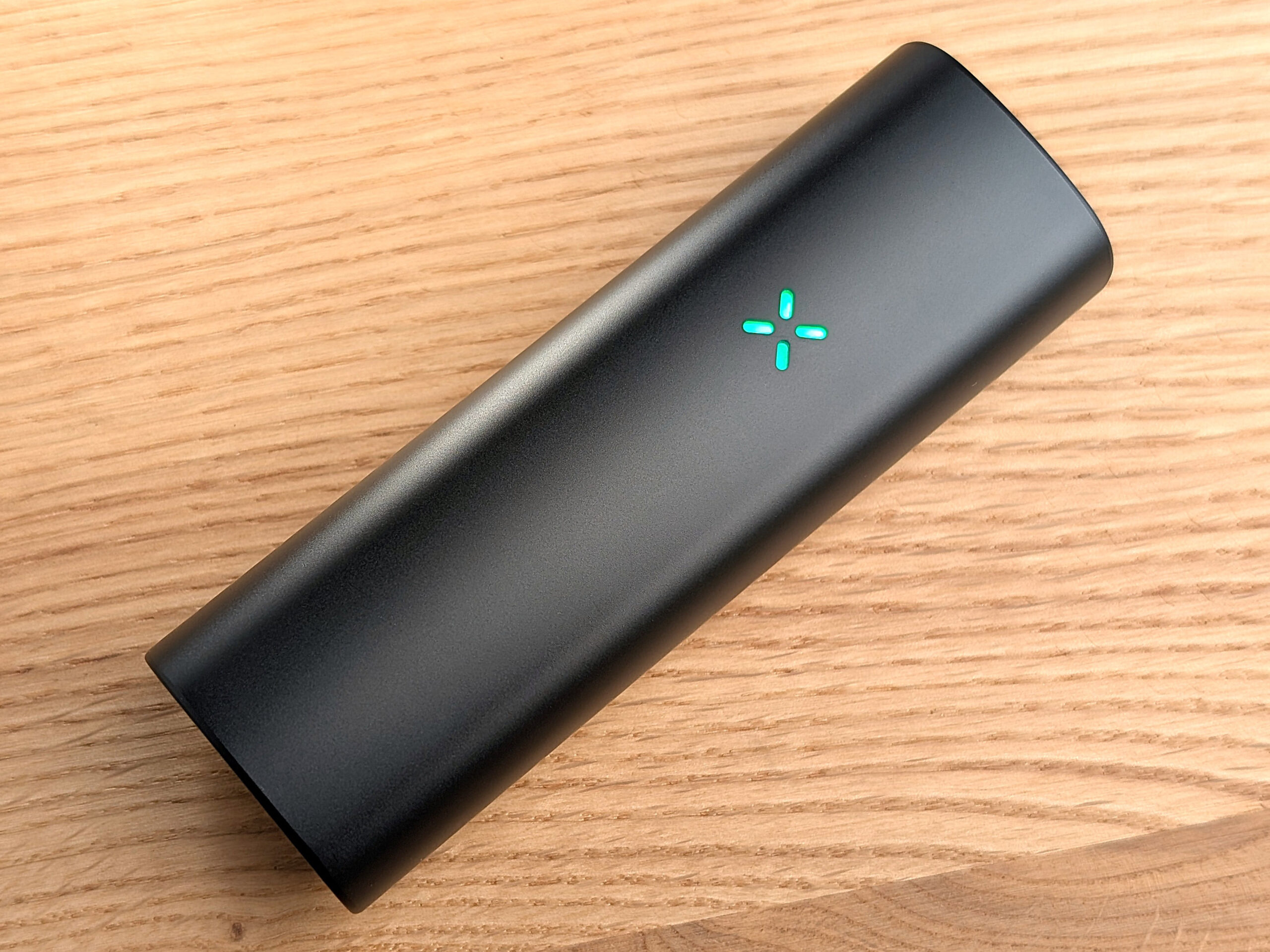 Ein Pax Mini liegt schräg auf einem Holztisch. Die Status LED leuchtet grün.