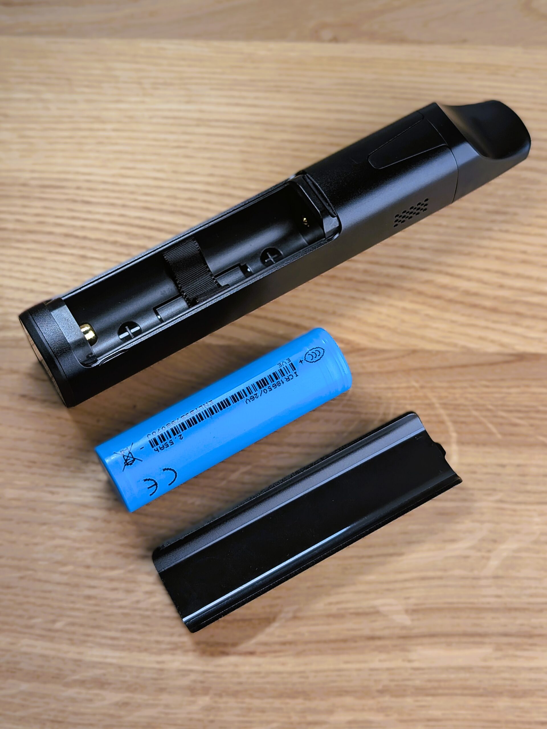 Der Cuboo Stick liegt mit der geöffneten Rückseite nach oben auf einem Holztisch. Daneben liegen der magnetisch schließende Deckel und die Batterie.