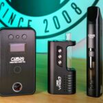 Ein Cuboo Heater Pro V2, ein Cuboo-VaGo-Vaporizer und ein Cuboo-Stick-Vaporizer stehen nebeneinander auf einem Holztisch. Im Hintegrund ist ein Teil des Verdampftnochmal-Logos ist im Hintergrund zu erkennen.