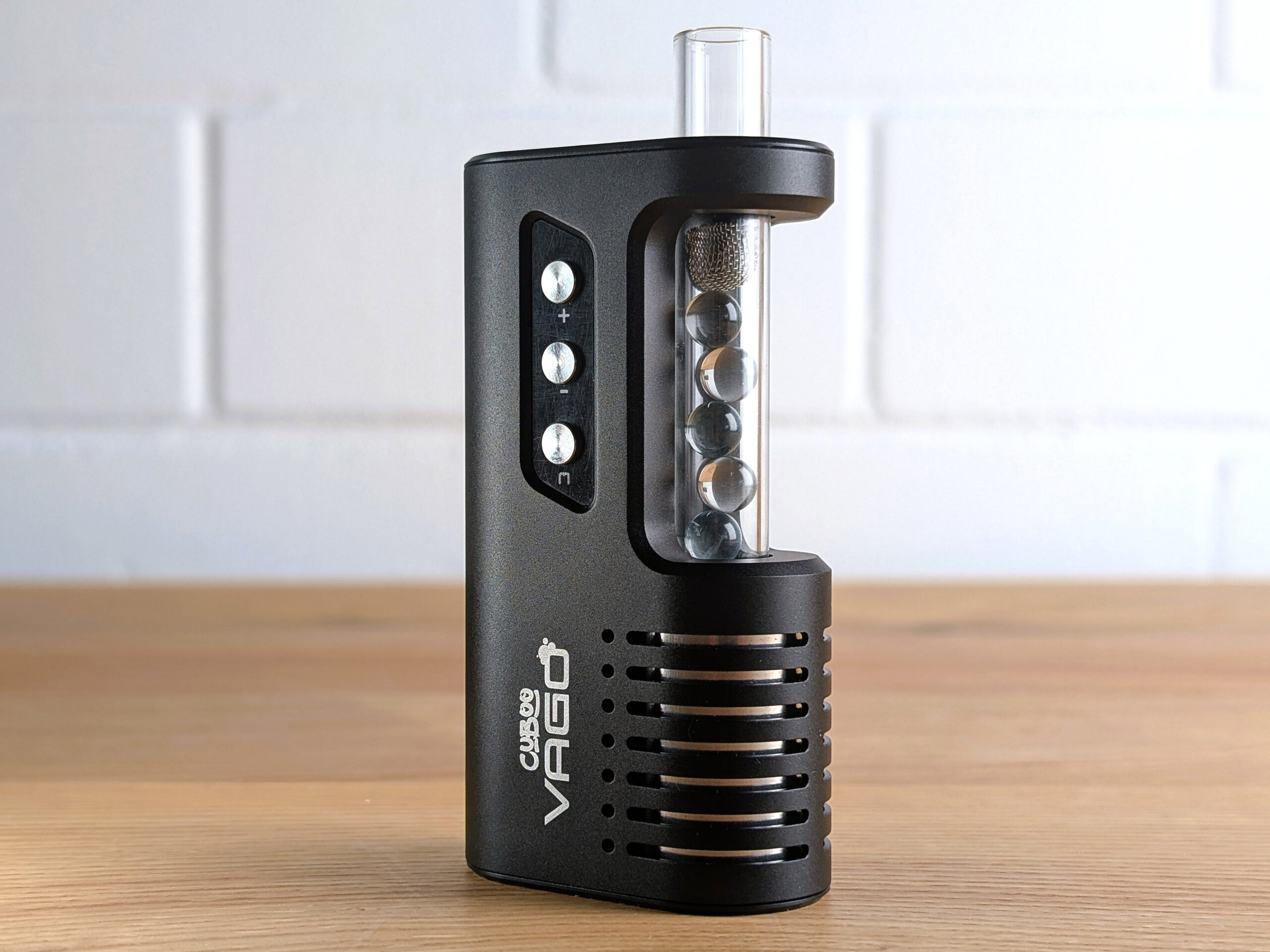 Der Cuboo-Vago-Vaporizer steht auf einem Holztisch. Das Gläserne Mundstück ist eingesteckt. Darin befinden sich sechs Glaskugeln, die durch ein Sieb im Mundstück gehalten weden.