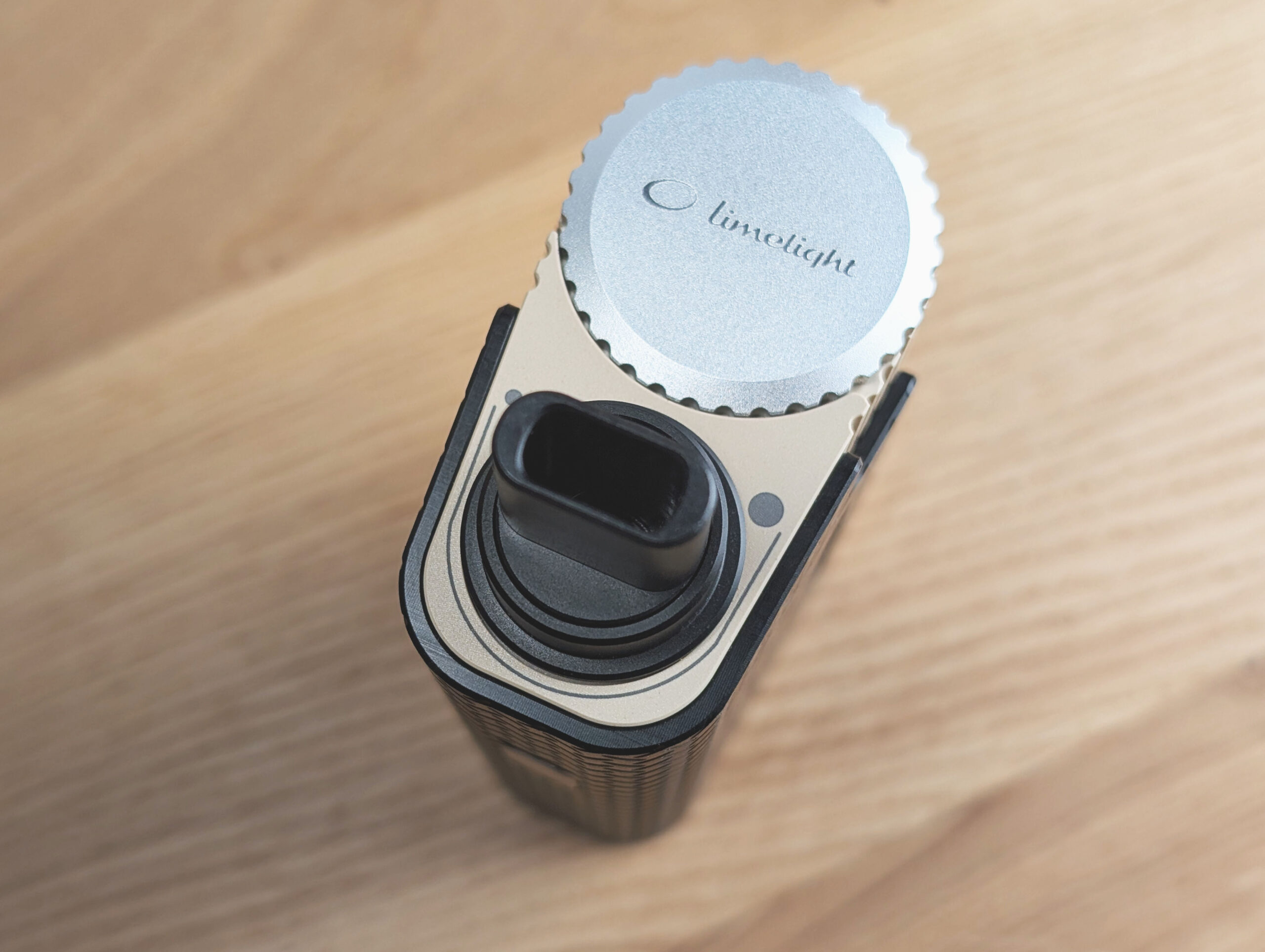 The Frolic Thermal Extractor on a wooden table. Top view showing the stainless steel screw and the cooling element with mouthpiece. Two dots on the cooling element indicate airflow direction.