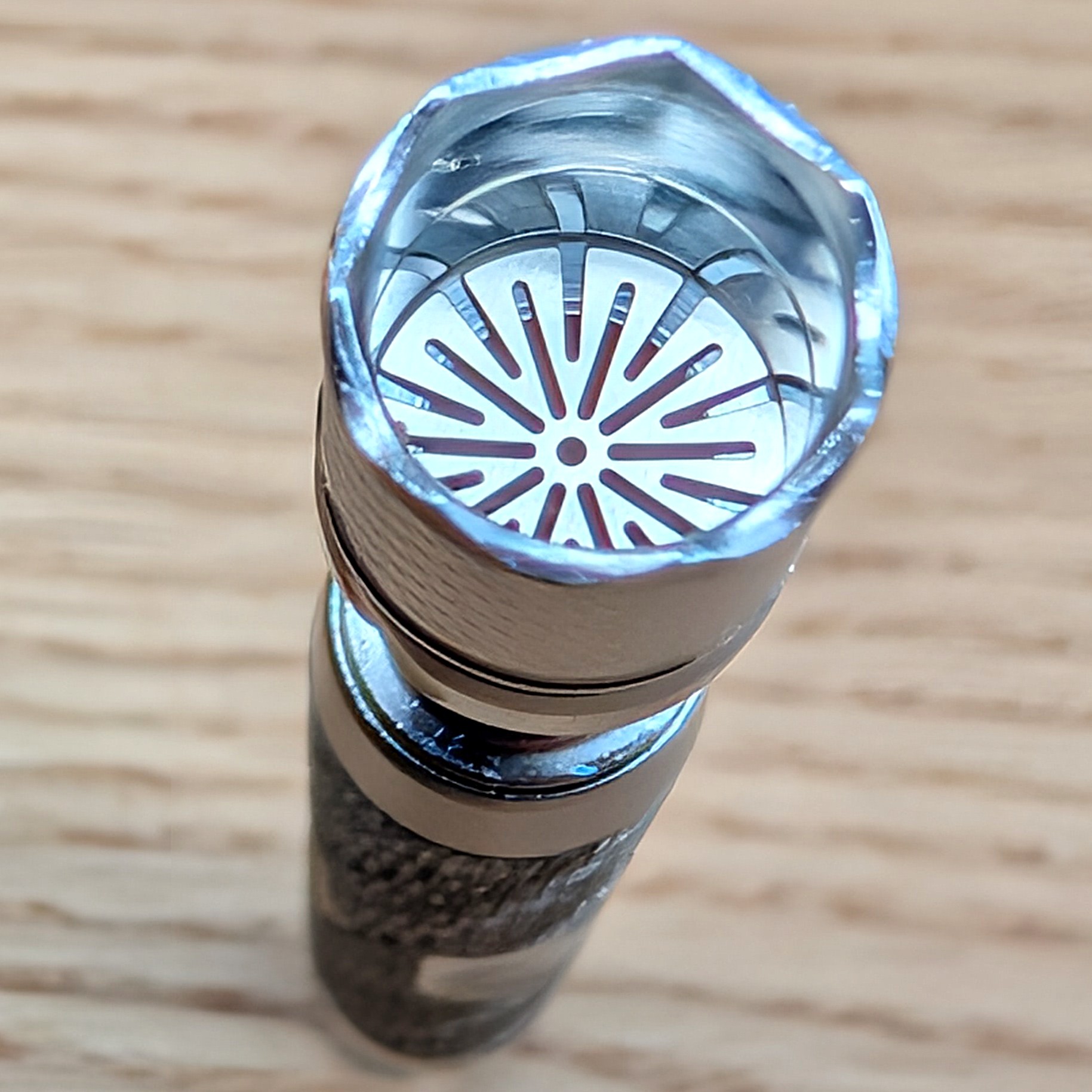 The photo shows a Dynavap M7 from above on a wooden table. The opened Dynavap reveals the inserted screen and the groove for the Adjust-a-Bowl.