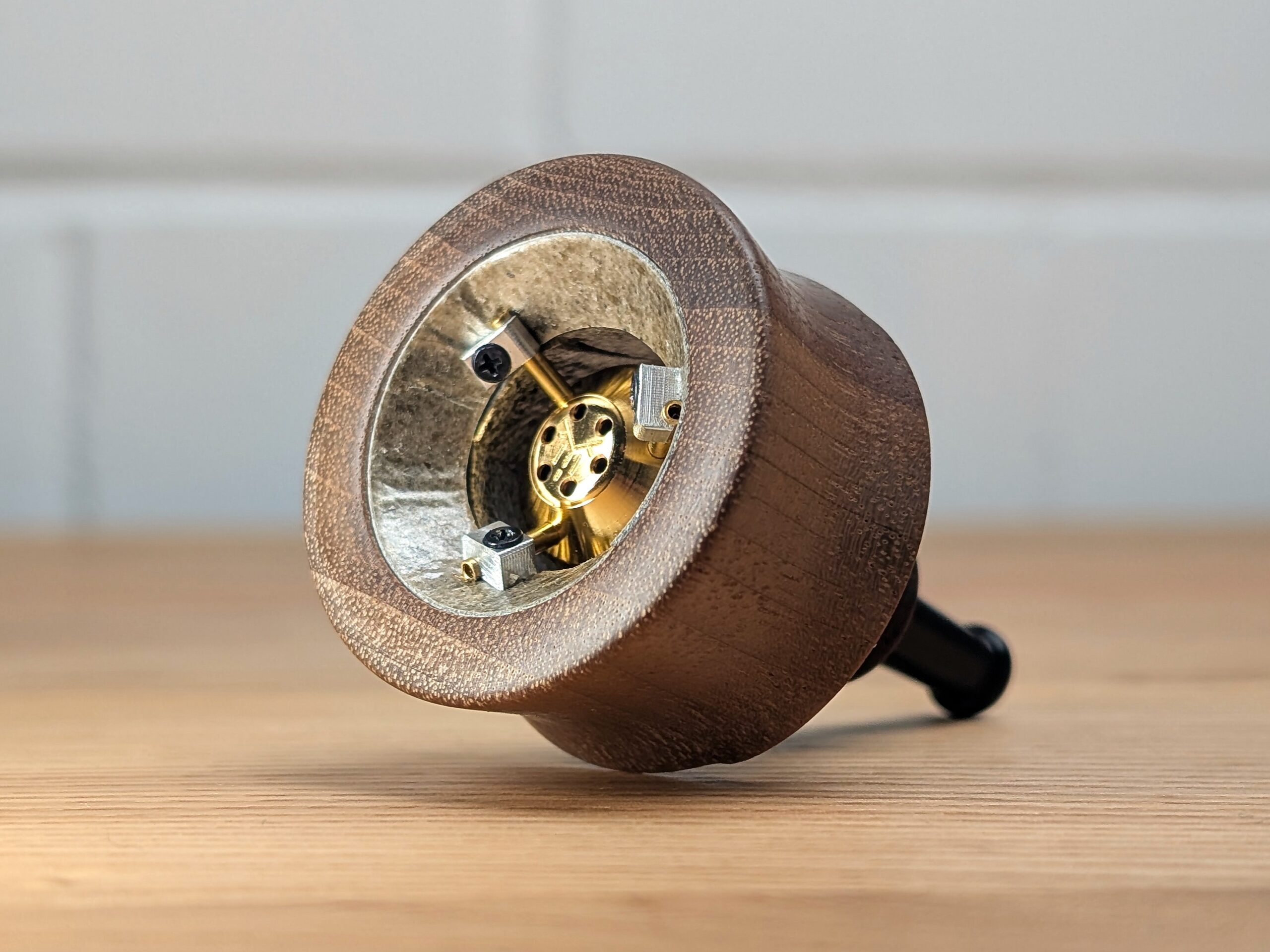 The VapMan vaporizer is standing on a wooden table. In the background, a blurred white brick wall is visible.