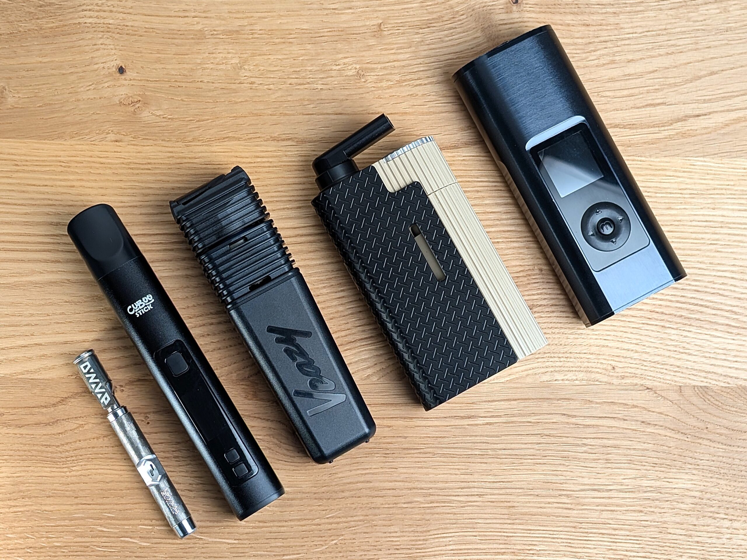 Fünf verschiedene Vaporizer liegen nebeneinander schräg auf einem Holztisch. Von links nach rechts: Dynavap M7XL, Cuboo, Veazy, Frolic, Arizer Solo V3