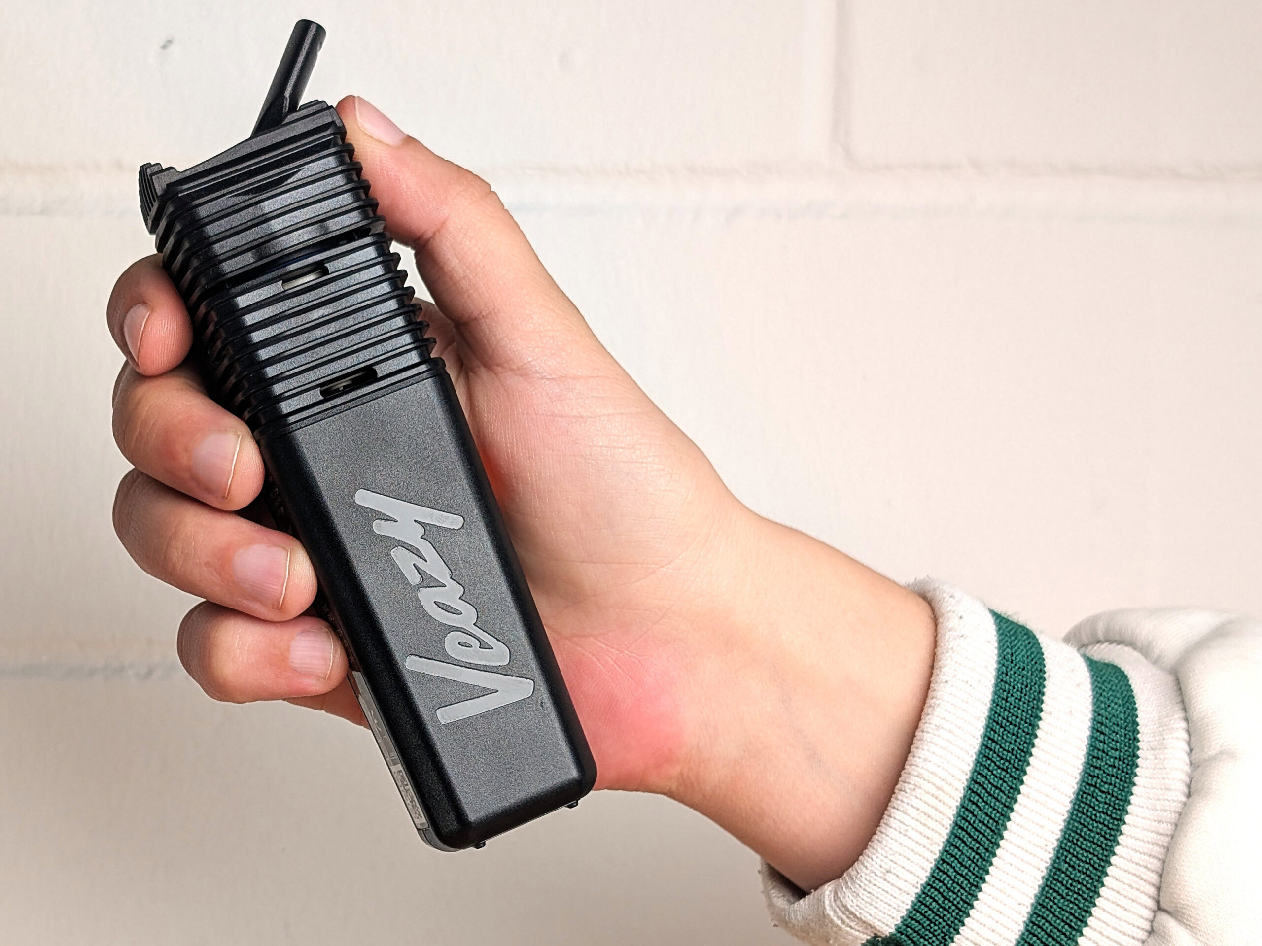 Hand holding a black portable vaporizer labeled ‘Veazy’ in front of a light-colored wall.