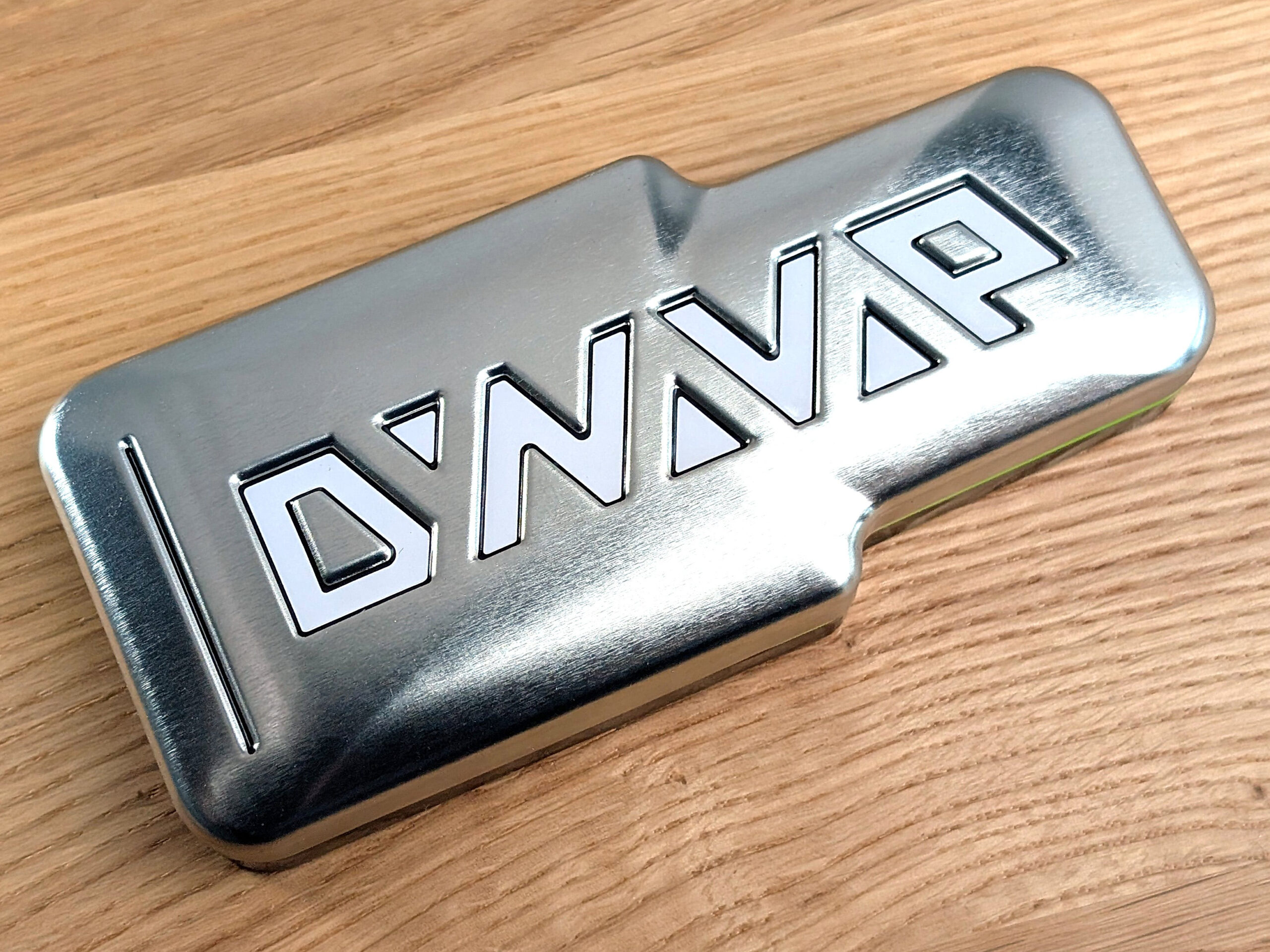 A closed DynaVap tin case on a wooden table.