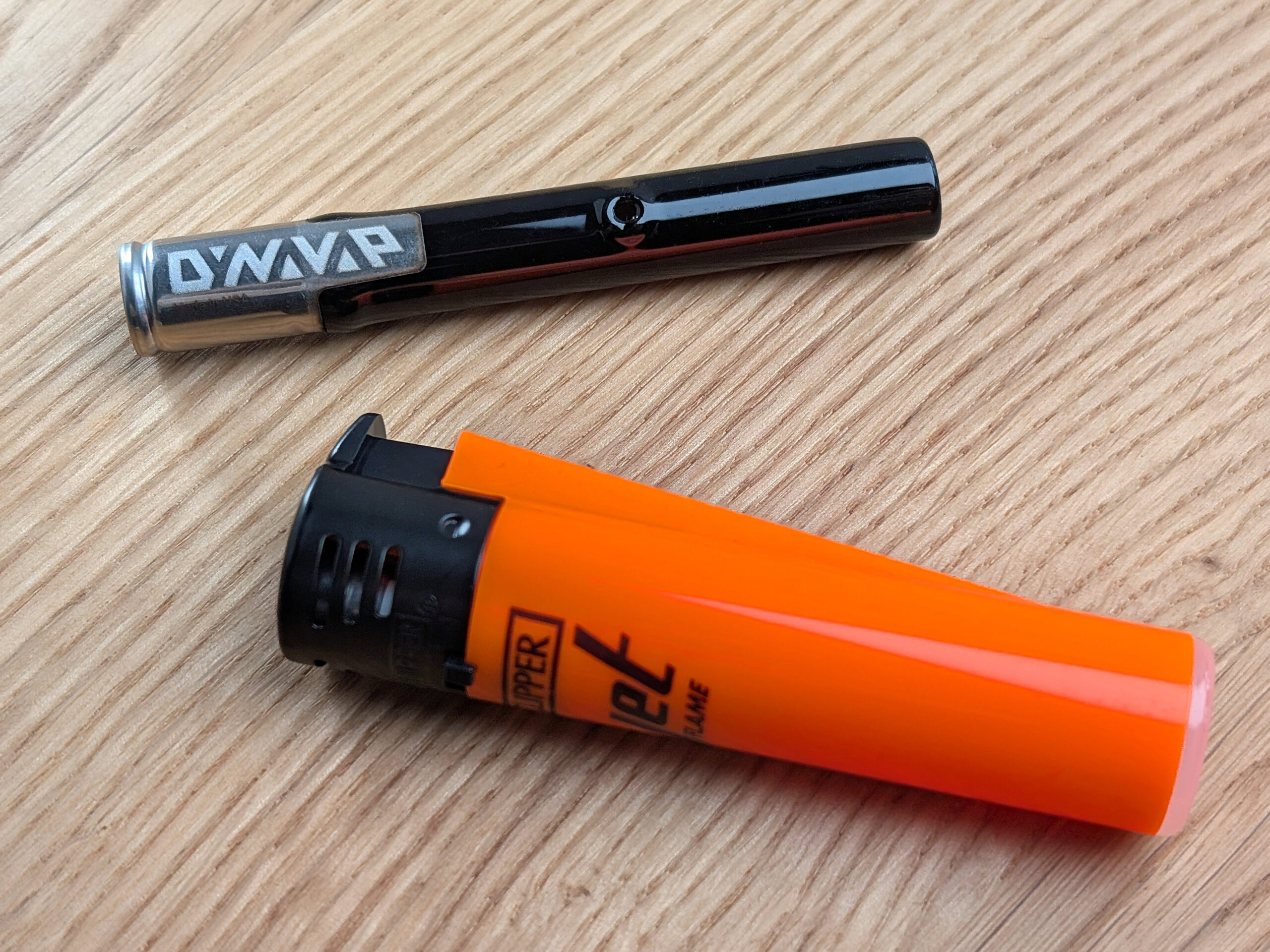 A Dynavap G3 vaporizer and an orange Clipper jet flame lighter on a wooden table.