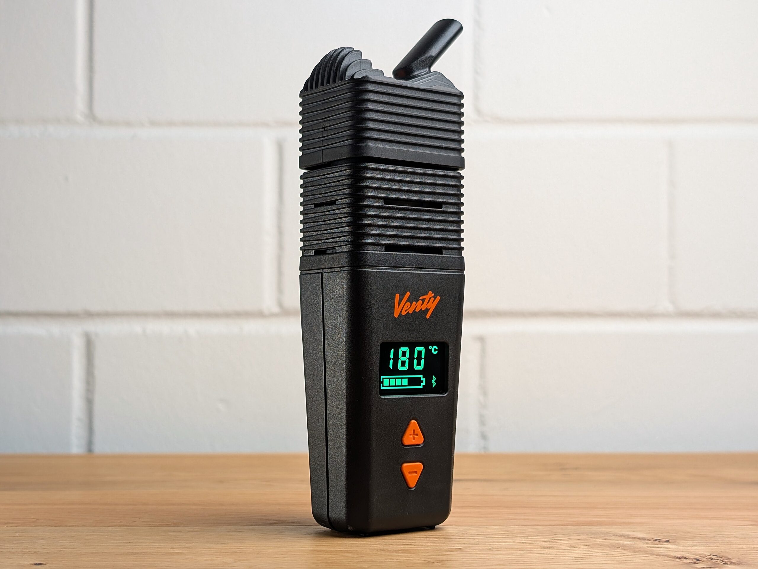 The Venty vaporizer standing on a wooden table. A blurred white brick wall is visible in the background.