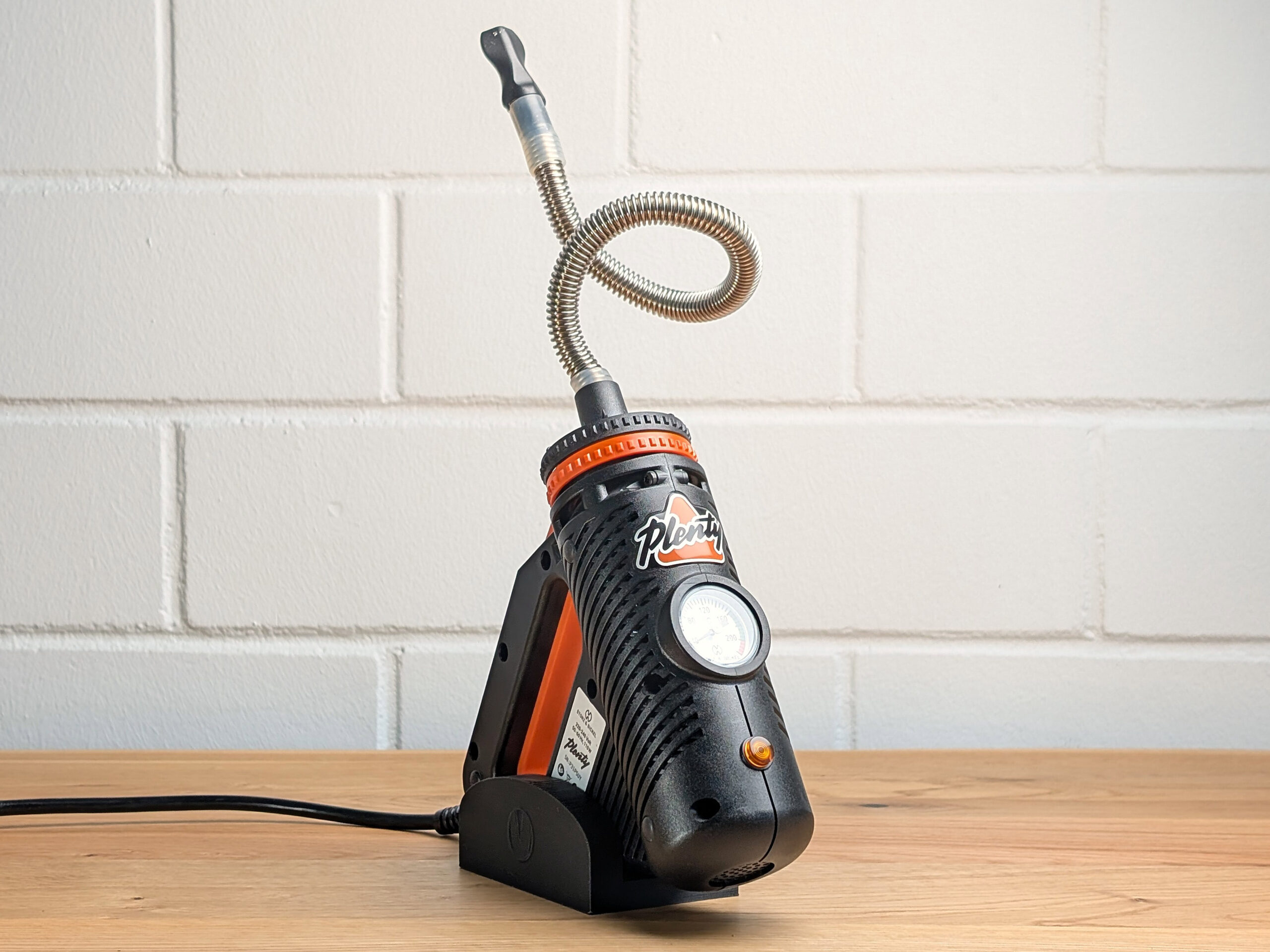 A Plenty Vaporizer on a wooden table, with a blurred white brick wall in the background.