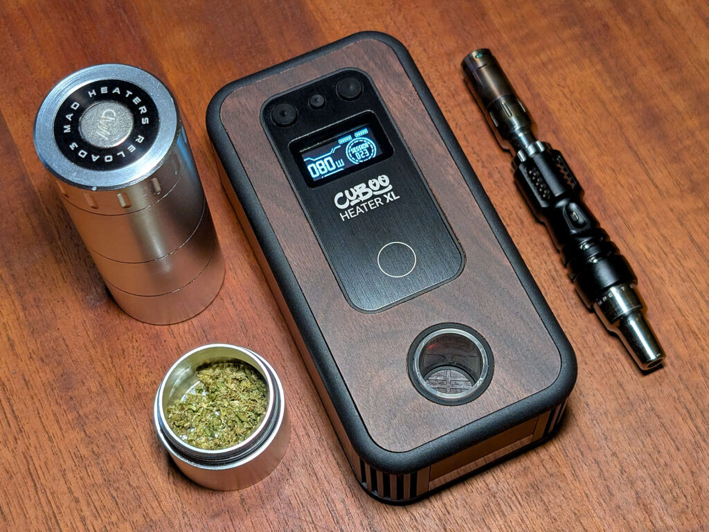 On a wooden table stands a Mad Heaters Reload 3, a Reload 3 Mini Pot filled with herbs, the Cuboo Heater XL, and a Tempest 2.