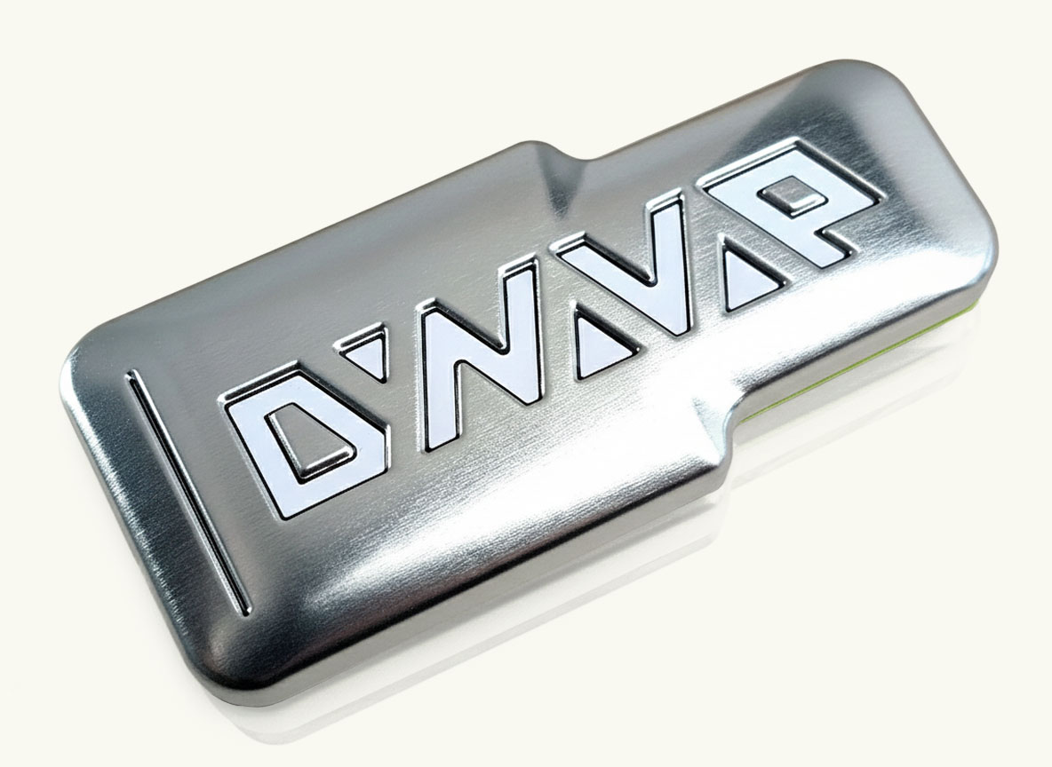 Ein flaches, silbernes Aufbewahrungsetui aus gebürstetem Metall mit großem, geprägtem „DYNAVAP“-Logo auf einem Holzuntergrund.