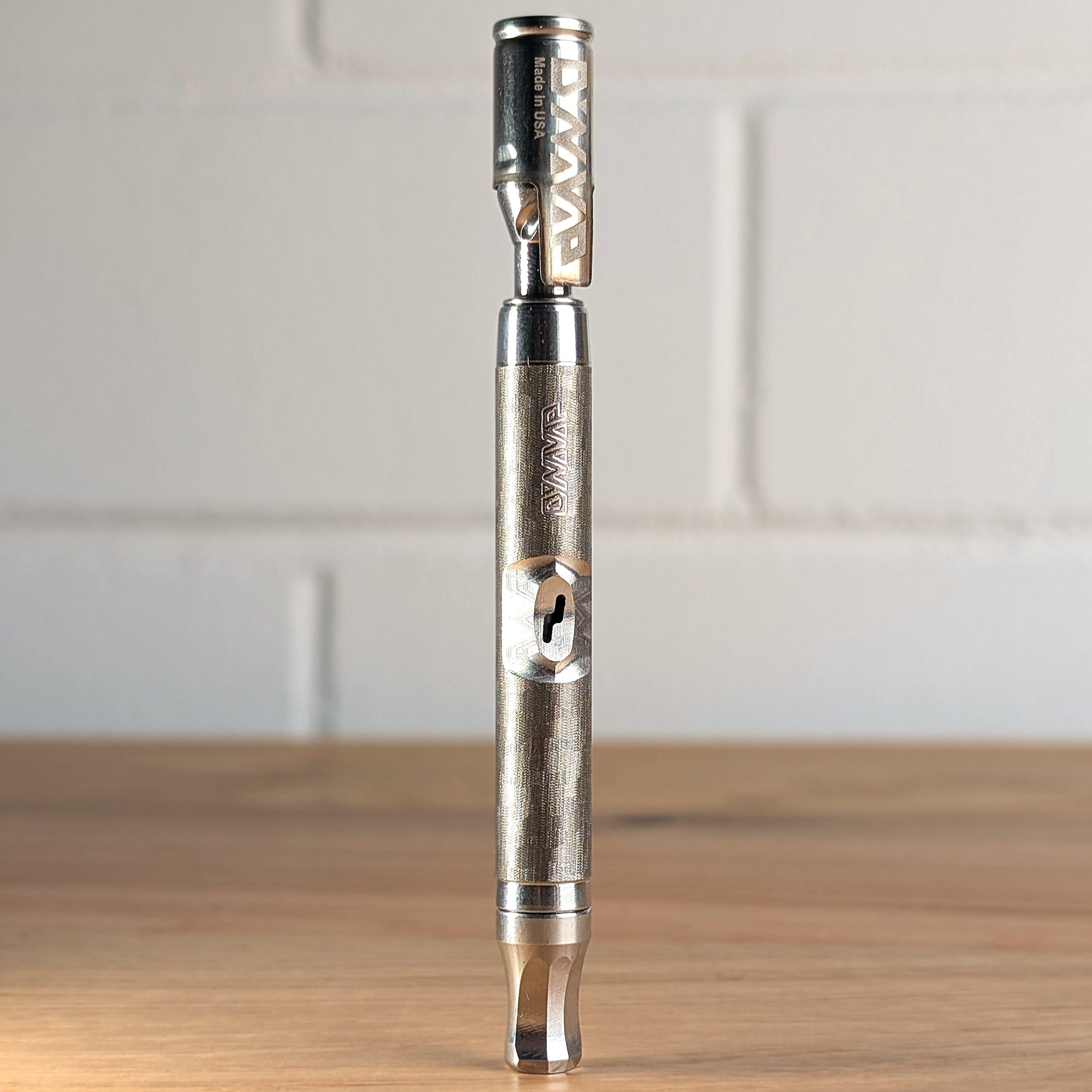 Der Dynavap Vaporizer steht auf einem Holztisch. Im Hintergrund ist eine unscharfe weiße Backsteinwand zu erkennen.